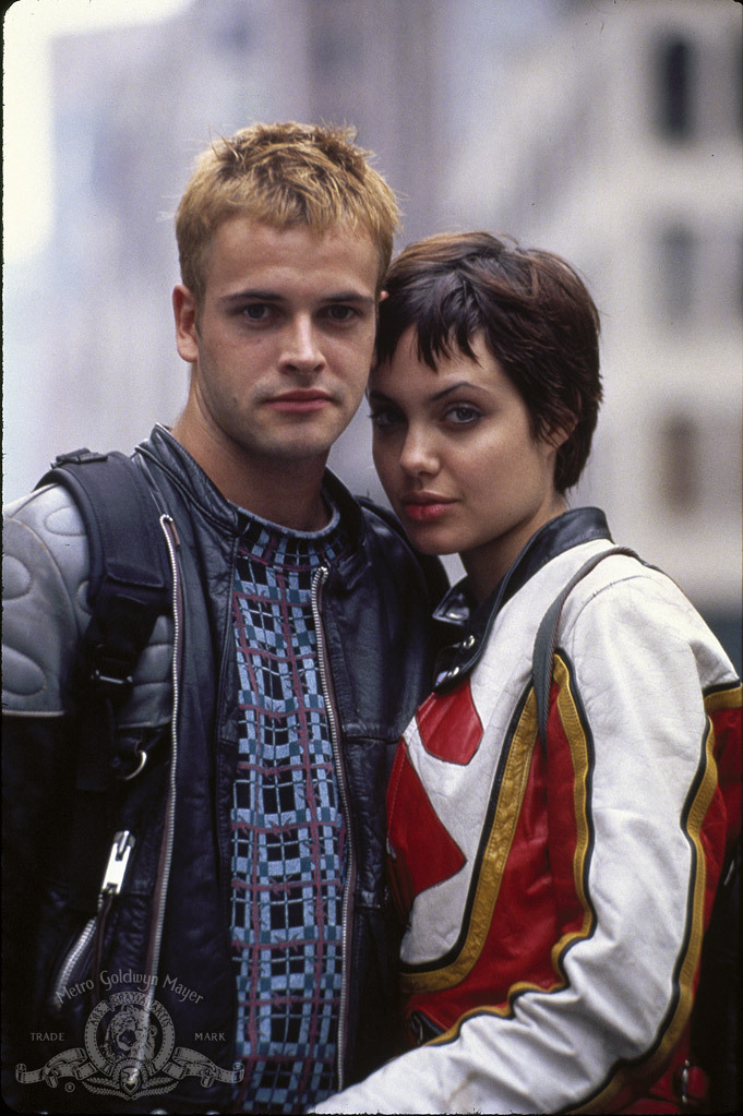 Uma foto promocional do filme Hackers: Piratas de Computador onde Jonny Lee Miller e Angelina Jolie posam juntos enquanto encaram sensualmene a câmera, demonstrando assim o relacionamento amoroso em que seus personagens se envolvem no filme. No canto inferior direito da imagem, está a marca d'água da produtora do filme, a MGM Studios (atualmente Amazon Studios)